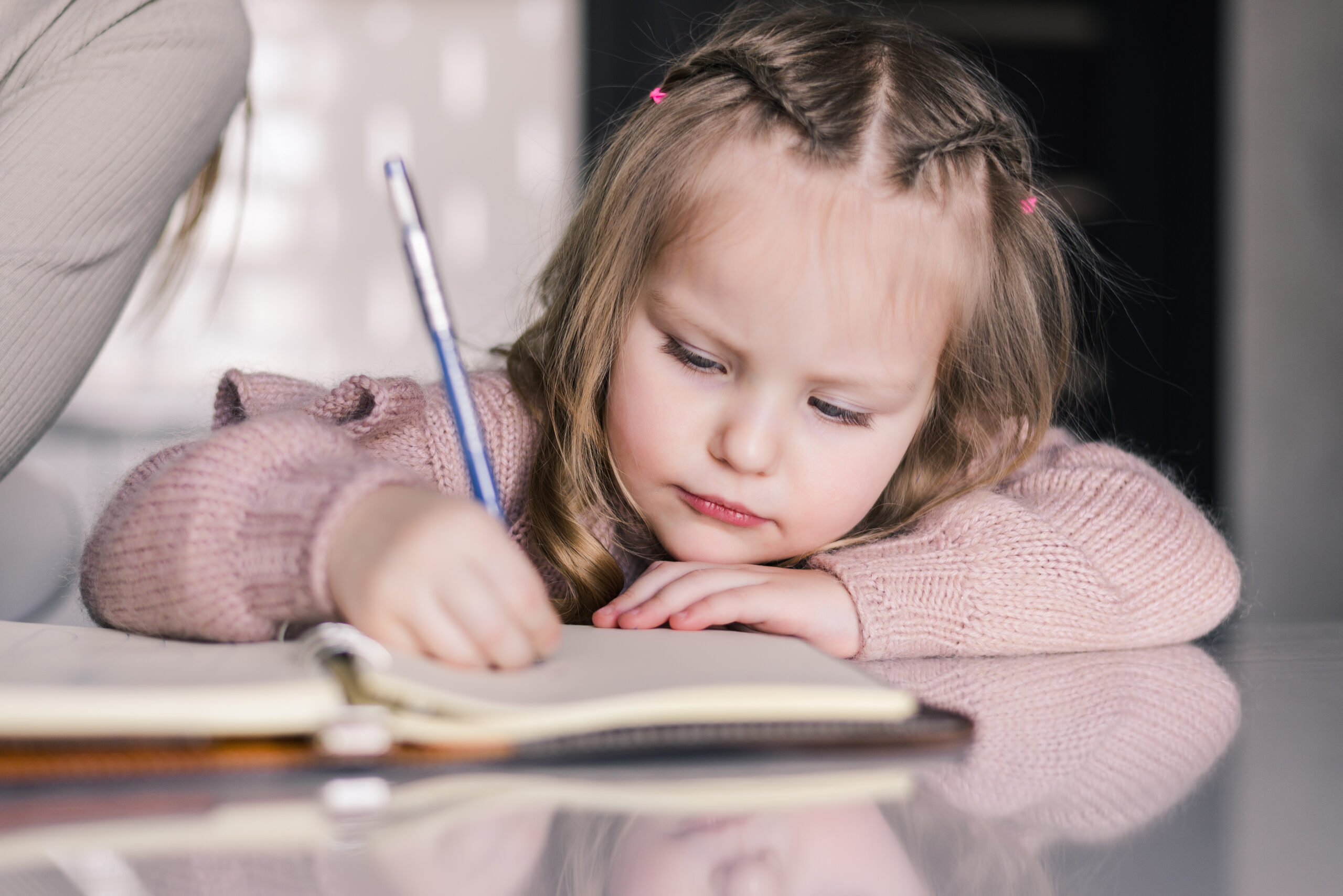 Adorable preschool girl drawing with pen at table. Cute daughter smiling and make kindergarten homework